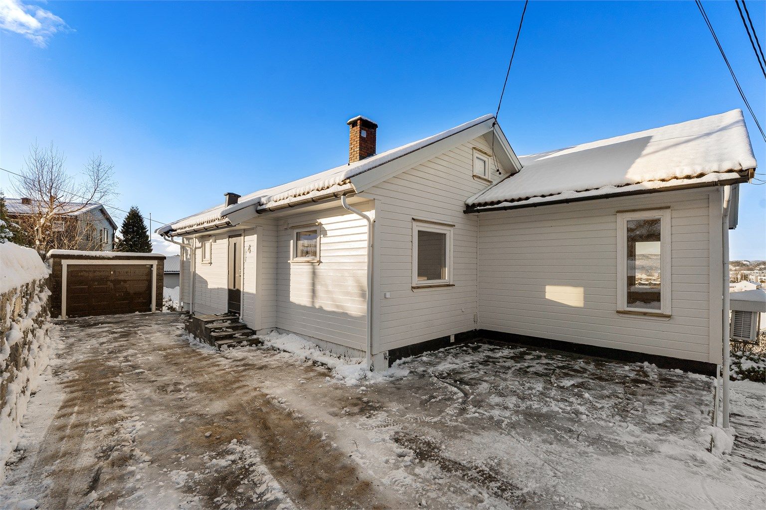 Fasade med god plass til parkering m.m. Det er også lagt opp til fremtidig el-bil lader ved husveggen.