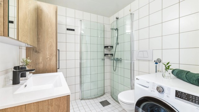 Badet har vegghengt servantinnredning med ovenpåliggende servant, speilskap med overlys samt vegghengt baderomsmøbel og toalett. Eget dusjhjørne med innfellbare glassdører. Det er opplegg for vaskemaskin og i tillegg plass til tørketrommel.