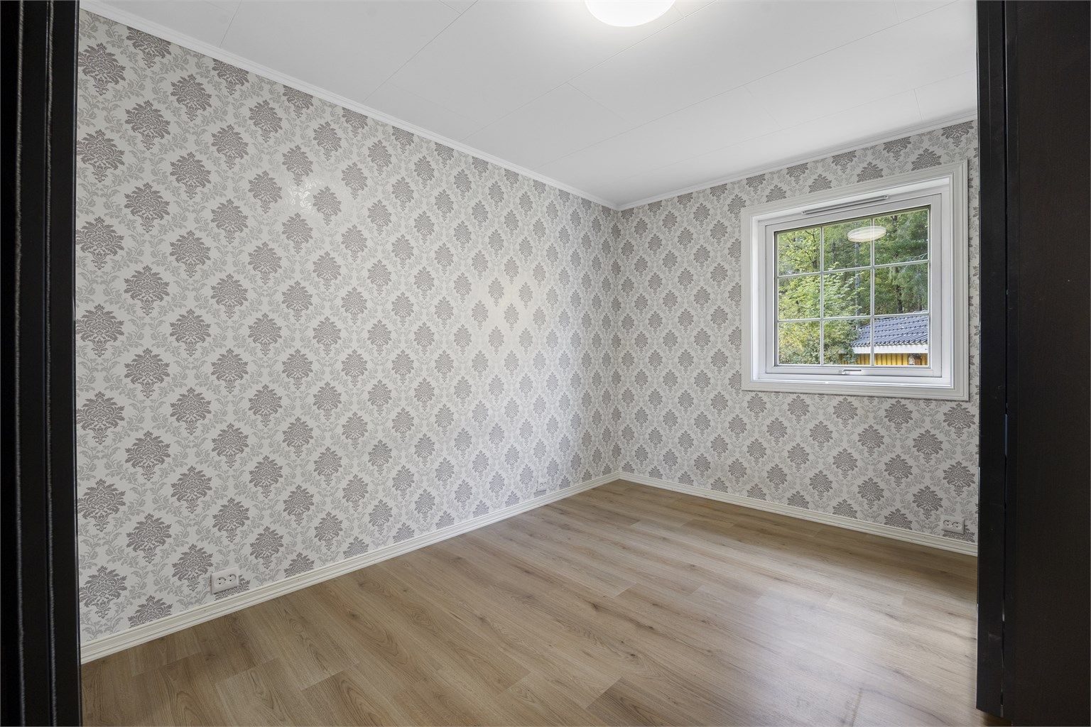 Romslig soverom i 1. etasje med laminatgulv og tapetserte vegger.