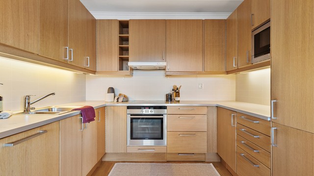 Åpen kjøkkenløsning. Innredning fra byggeår. Glatte fronter. Benkeplate med laminert overflate. Kjøkkenvask med armatur. Stikkontakt over kjøkkenbenk. Integrert stekeovn, platetopp, oppvaskmaskin og kjøleskap med fryser.