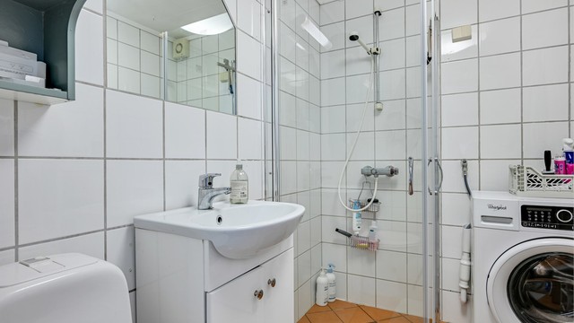 Flislagt bad i leiligheten med dusjhjørne i glass og opplegg for vaskemaskin.