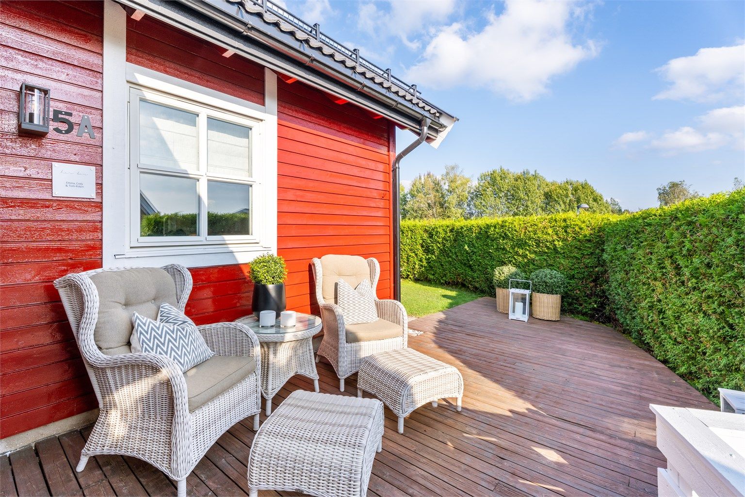 Terrassen har gulvflate belagt med terrassebord og omkranses av tett hekk.