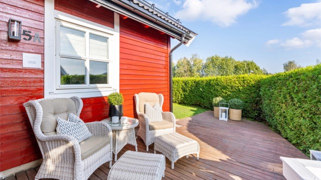 Terrassen har gulvflate belagt med terrassebord og omkranses av tett hekk.