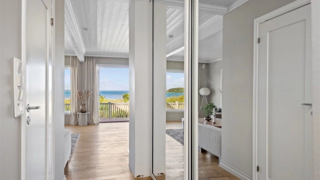 Entreen ligger åpen mot stuen, slik at det første man ser er den nydelige sjøutsikten via store stuevinduer. Entreen har også en stor skyvedørsgarderobe med speilfronter langs den ene siden og inngang til badet på den andre.
