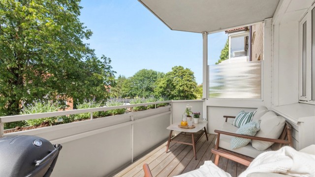 Den vestvendte balkongen vender mot frodige fellesarealer og blir en naturlig forlengelse av stuen gjennom de varme månedene.