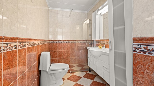 Badet er utstyrt med gulvstående toalett, servantinnredning og dusjnisje med glassvegg.