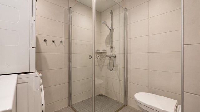 Flislagt gulv og vegger med moderne lyse fliser, innfellbare dusjvegger i herdet glass.