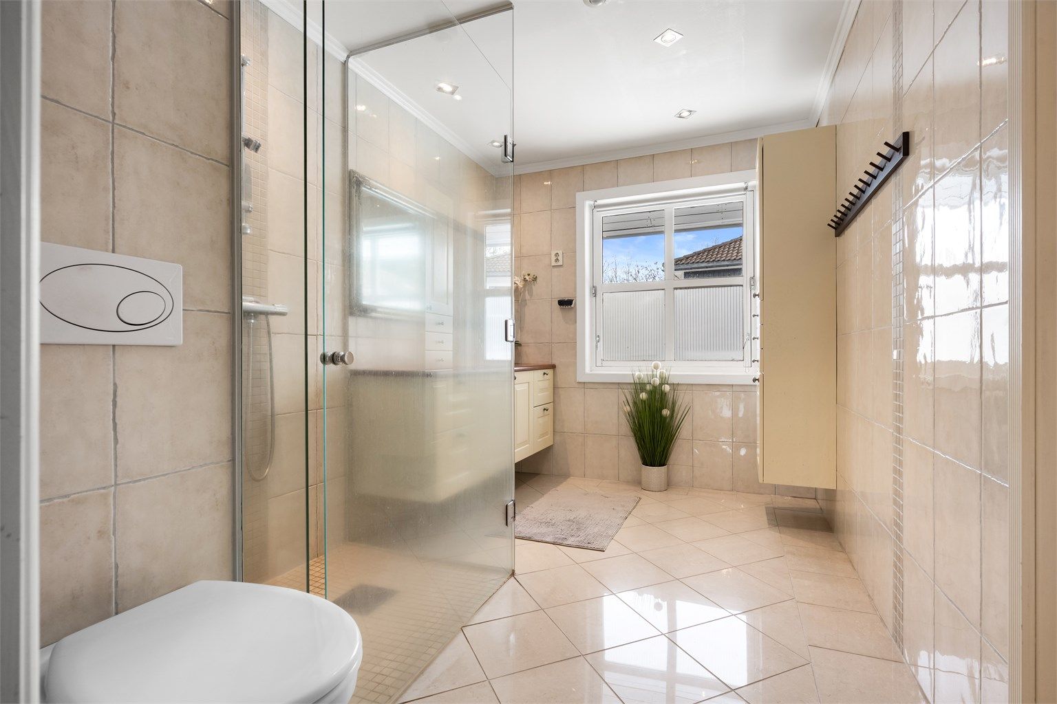 Baderom fra vurdert til å være fra 2005 (datostemplet avløpsrør i sluk). Det er flislagt gulv med varme og flislagte vegger, himling med malt slett flate og downlights, og vegghengt servantskap med profilerte fronter. 