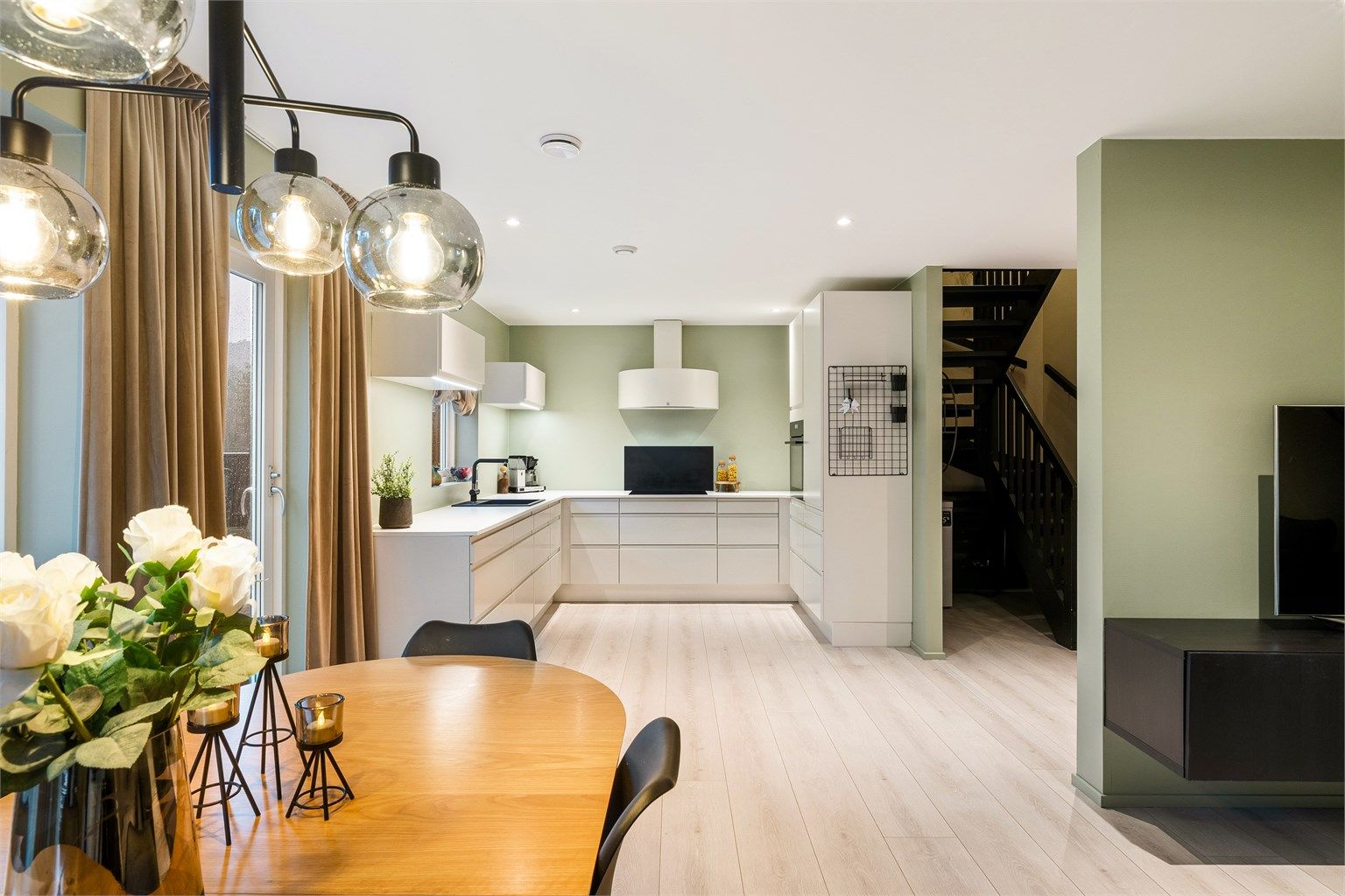 Åpent kjøkken med lyse overflater og grønn bakvegg som gir rommet en luftig, moderne følelse og fin flyt mot spisestuen.