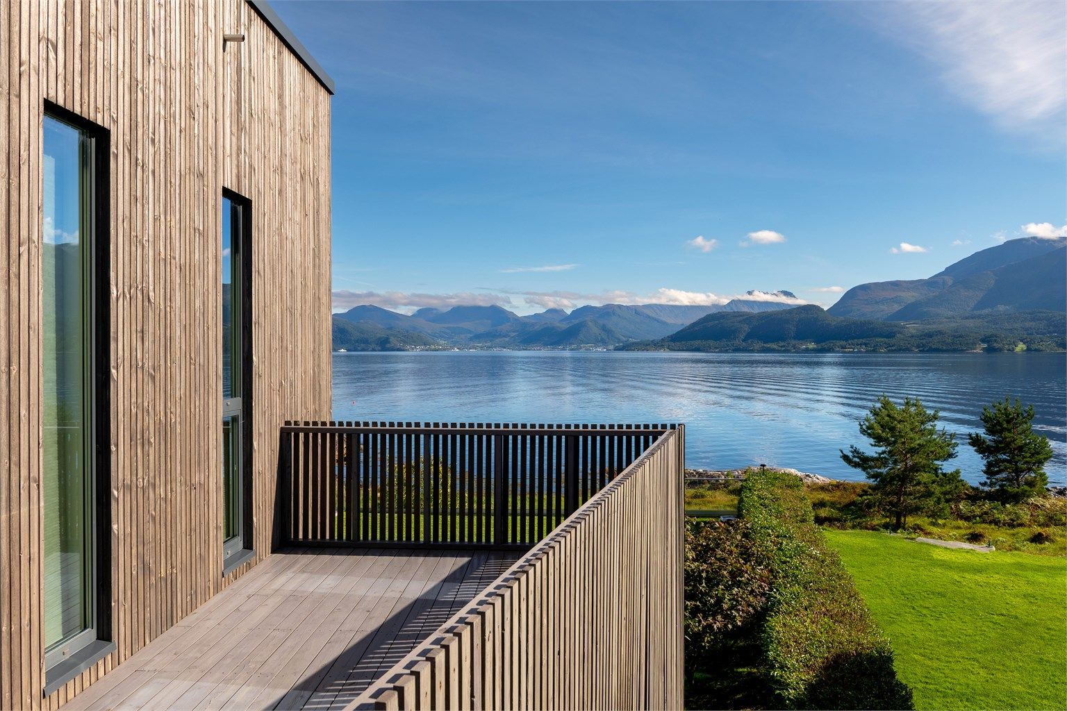 Sørvestvendt balkong med rekkverk av tre og trappeadkomst ned til terrenget.