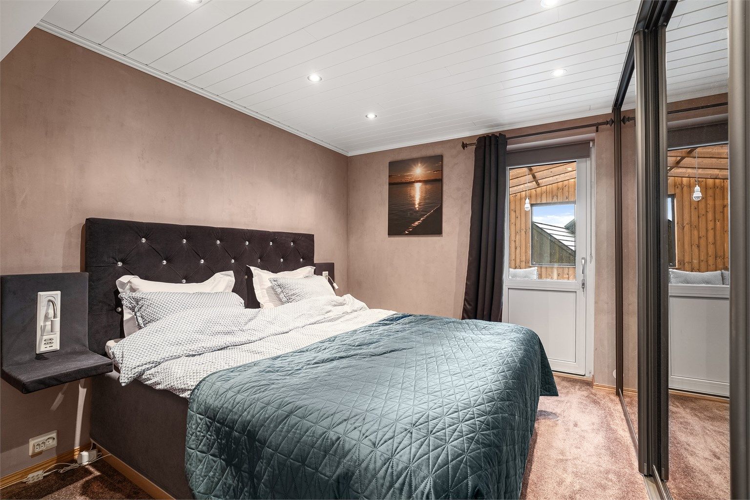 Hovedsoverom med vegg-til-vegg teppe, jordfarger på veggene og med skyvedørsgarderobe. Det er utgang til utestuen fra dette rommet. 