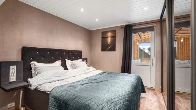 Hovedsoverom med vegg-til-vegg teppe, jordfarger på veggene og med skyvedørsgarderobe. Det er utgang til utestuen fra dette rommet.