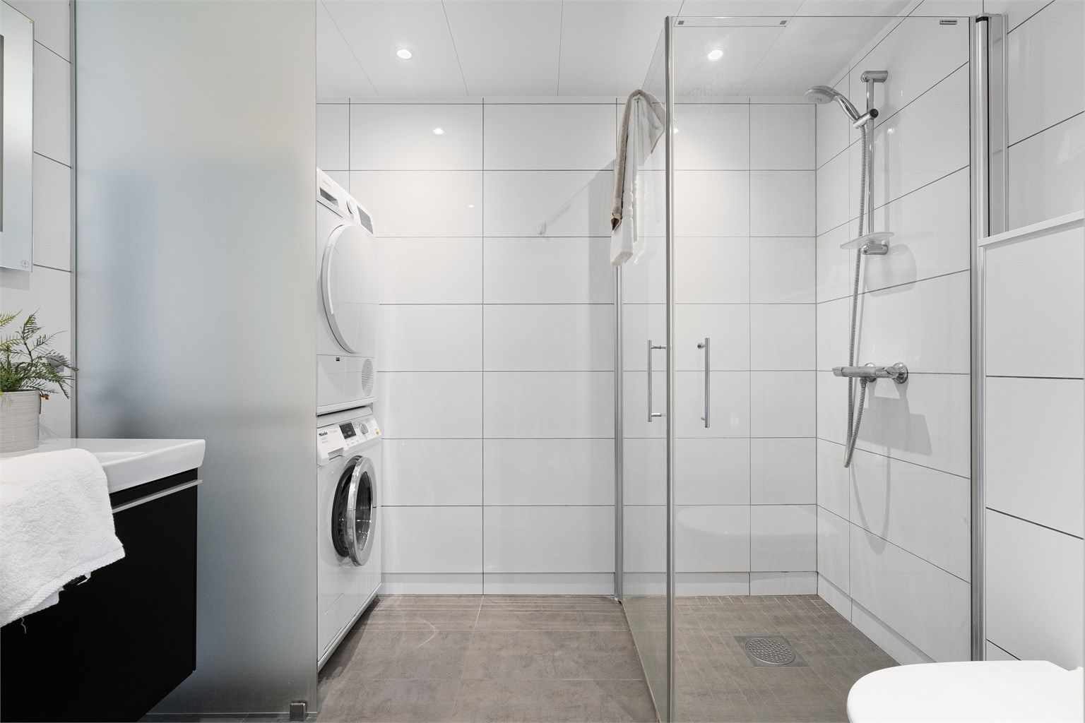 Det er dusjhjørne med innfellbare dører, vegghengt toalett og servant med oppbevaringsplass i skuffer.  Opplegg for vaskemaskin og plass til tørketrommel, som er smart plassert bak en frostet glassvegg. Spotter i tak