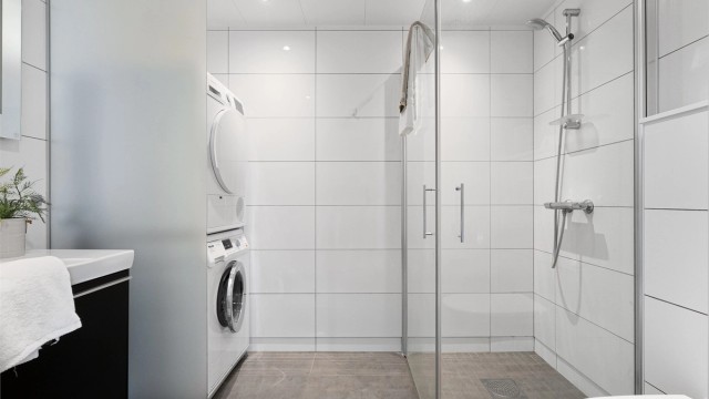 Det er dusjhjørne med innfellbare dører, vegghengt toalett og servant med oppbevaringsplass i skuffer. Opplegg for vaskemaskin og plass til tørketrommel, som er smart plassert bak en frostet glassvegg. Spotter i tak