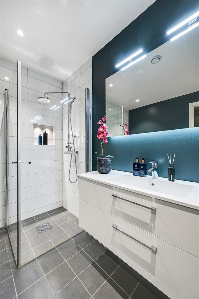 Rommet har innredning med heldekkende servant, veggmontert toalett og dusjvegger/hjørne. 