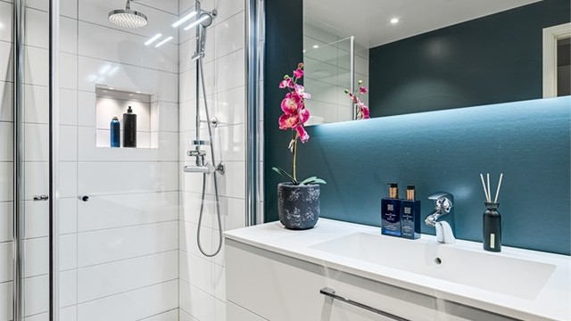 Rommet har innredning med heldekkende servant, veggmontert toalett og dusjvegger/hjørne.