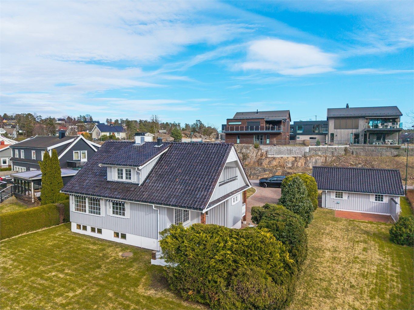 Eneboligen ligger på en flat tomt med hage, og har stående bordkledning og tak tekket med glasert takstein.