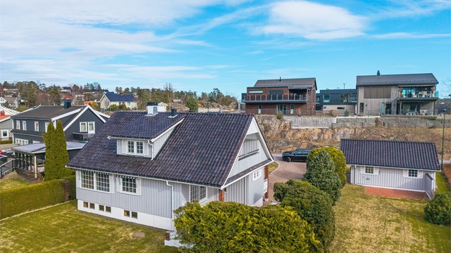 Eneboligen ligger på en flat tomt med hage, og har stående bordkledning og tak tekket med glasert takstein.