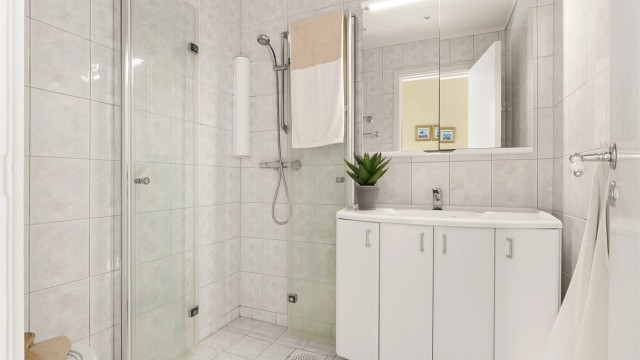 Fliselagt bad med varme i gulv, dusjhjørne med dører, vegghengt servantinnredning og speil med lys. Badet er vurdert til å være delvis oppgradert i 1995.
