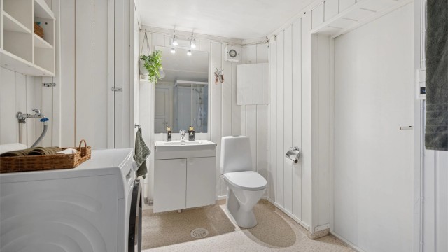 Badet i kjelleretasjen har gulvbelegg med gulvvarme, vegghengt servantinnredning, dusjkabinett, gulvstående toalett og opplegg for vaskemaskin.
