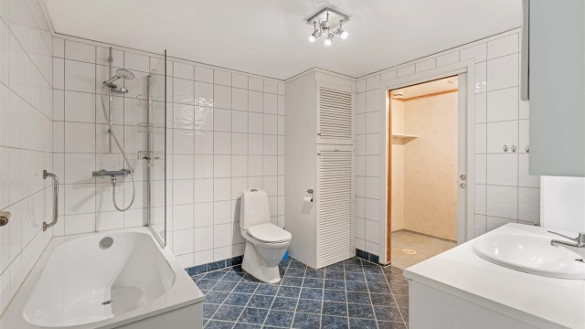 Romslig, helfliset bad med badekar, servantinnredning og toalett.
