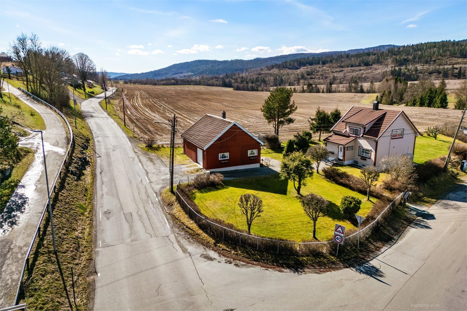 En klassisk enebolig fra 1936 med en stor, separat uthusbygning, beliggende på en tilnærmet flat tomt i landlige omgivelser.
Foto: Haiman Askari