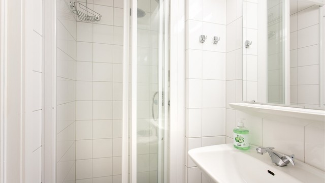 Dusjhjørne med innfellbare glassdører og flislagte vegger.