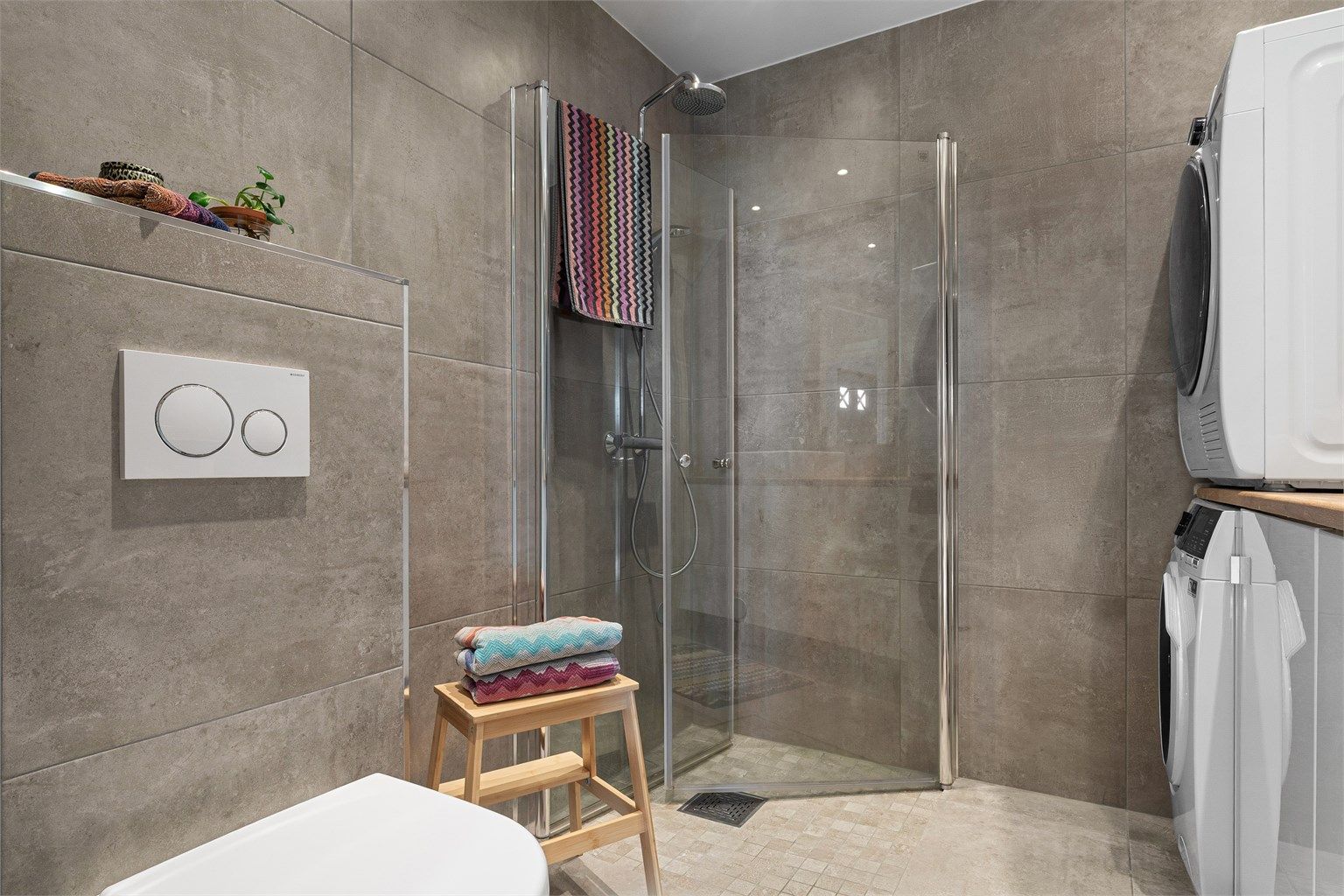 Badet er også innredet med vegghengt toalett og dusjhjørne med innfellbare glassvegger, hånd- og regnfallsdusj. Det er i tillegg opplegg til vaskemaskin.