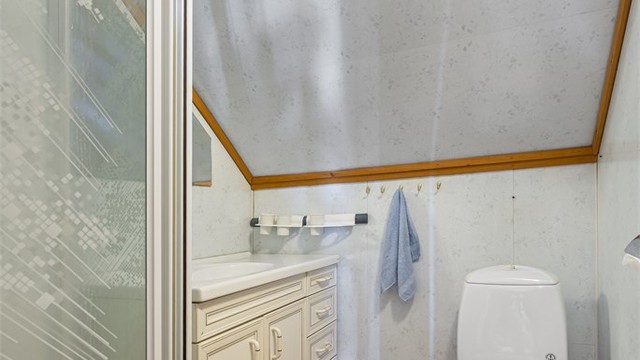 Badet på loftet har dusjnisje, gulvstående toalett og baderomsplater på veggene.