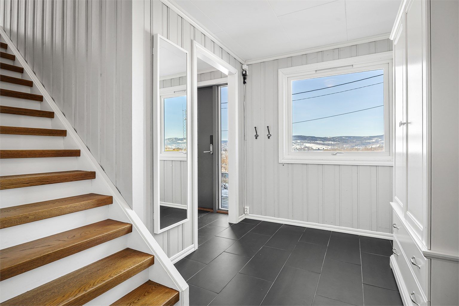 Velkommen inn i underetasjens entré/gang med flislagt gulv og trapp opp til hovedetasjen.