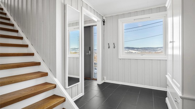 Velkommen inn i underetasjens entré/gang med flislagt gulv og trapp opp til hovedetasjen.