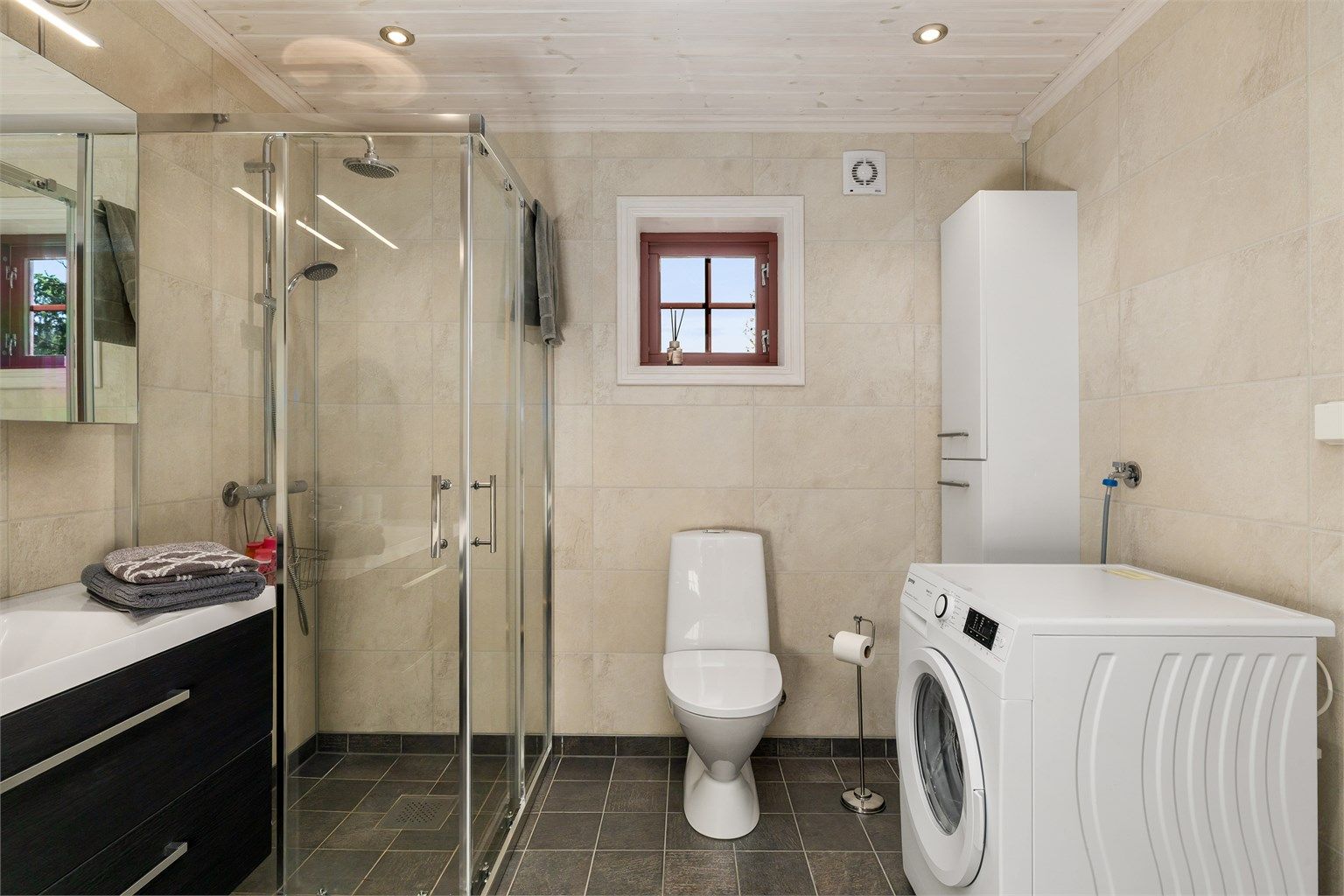 Badet har dusjnisje med glassdører og opplegg for vaskemaskin.