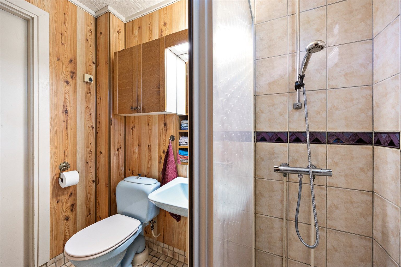 Badet har dusjvegg med skyvedør innredet med flislagte gulv og vegger