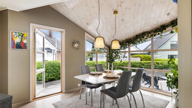 Store vindusflater gir rikelig med naturlig lys til spiseplassen. Her er det utgang til terrasse og uteplass på fremsiden av boligen.