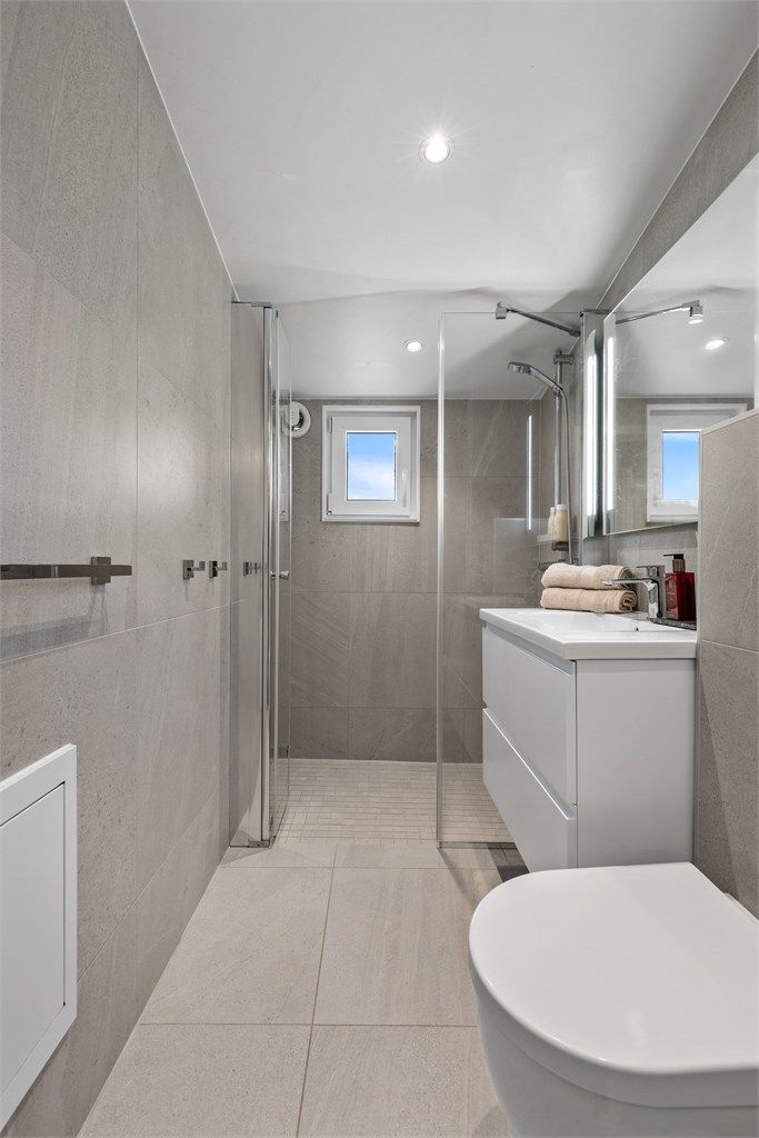 Dusjnisje med glassvegg og glassdør. Vegghengt toalett. Mekanisk avtrekksvifte i vegg.