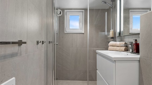 Dusjnisje med glassvegg og glassdør. Vegghengt toalett. Mekanisk avtrekksvifte i vegg.