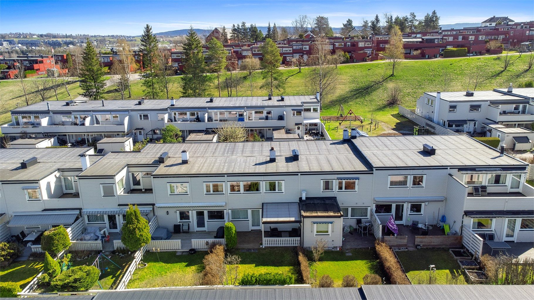 Fine fellesarealer med gressplener og lekeapparater mellom boligrekkene.