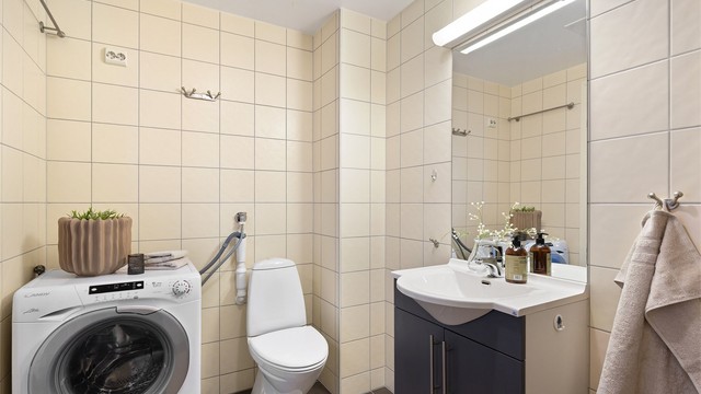 Rommet er utstyrt med vegghengt servantinnredning, speil med overlys, dusjhjørne, mekanisk avtrekk og opplegg for vaskemaskin.