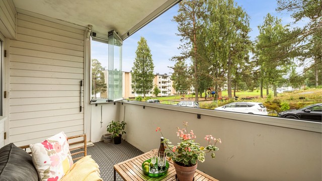 Sydvendt og romslig innglasset balkong med luftig utsyn mot fellesområdet og lekeplassen.