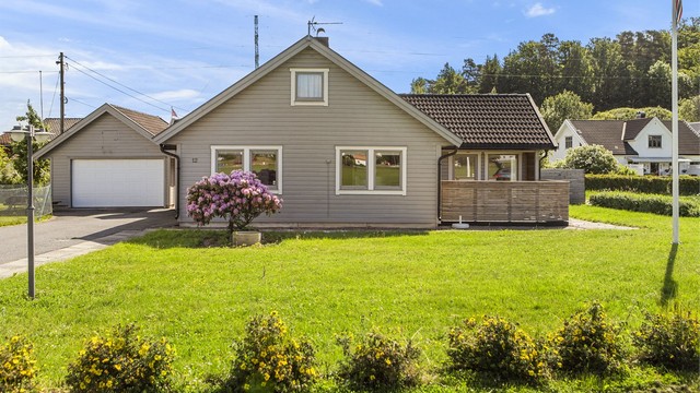 Eneboligens fasade sett fra hagen, med en stor rhododendronbusk.