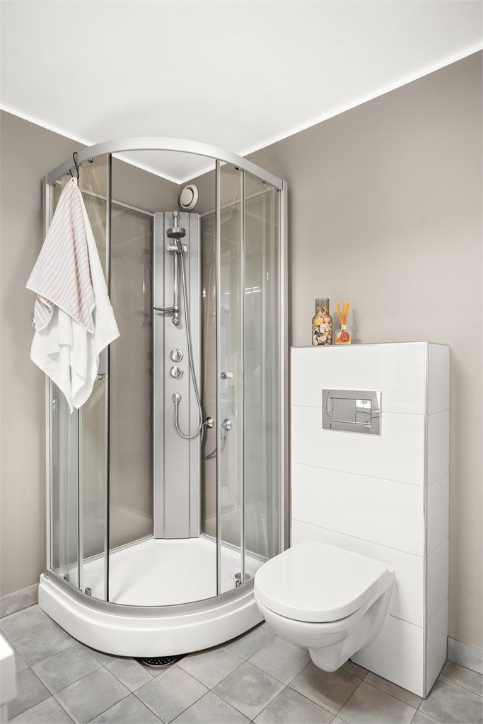 Badet er utstyrt med dusjkabinett med skyvedører i glass og vegghengt toalett med innebygget sisterne.
