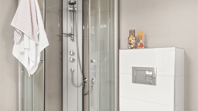 Badet er utstyrt med dusjkabinett med skyvedører i glass og vegghengt toalett med innebygget sisterne.