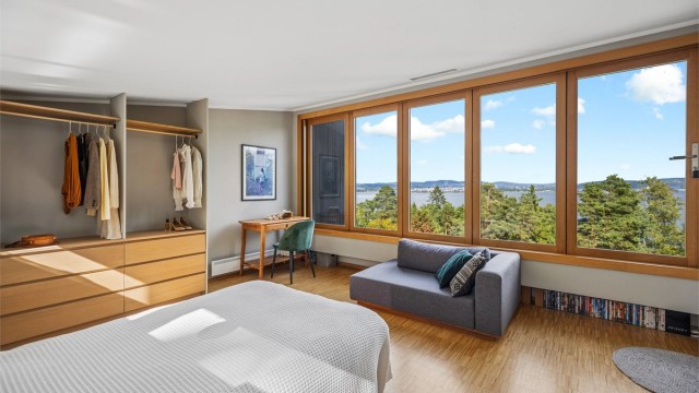Et romslig og lyst soverom (opprinnelig godkjent til stue) med smart garderobeløsning, skrivebord og en slående utsikt mot Bunnefjorden og furuskogen.
