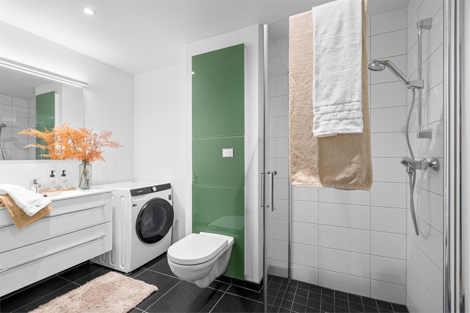 
Fint bad av godt størrelse med varme i gulv, fliser på gulv og i dusjsone. Det er dusjhjørne med innfellbare dører, vegghengt toalett og servant med oppbevaringsplass i skuffer. Stort speil på vegg. 
