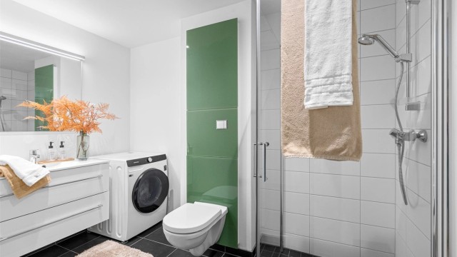 Fint bad av godt størrelse med varme i gulv, fliser på gulv og i dusjsone. Det er dusjhjørne med innfellbare dører, vegghengt toalett og servant med oppbevaringsplass i skuffer. Stort speil på vegg.