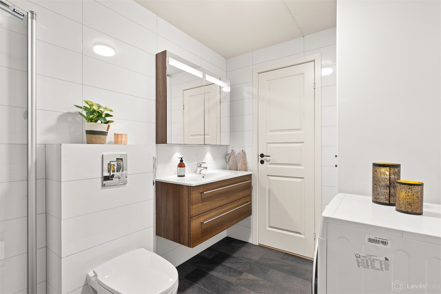 Badet er innredet med vegghengt toalett, servantinnredning med ovenpåliggende servant og armatur, speilskap med overlys og stikkontakt, samt gulvstående høyskap med god oppbevaringsplass. Dusjhjørne med innfellbare dører, samt opplegg til vaskemaskin.