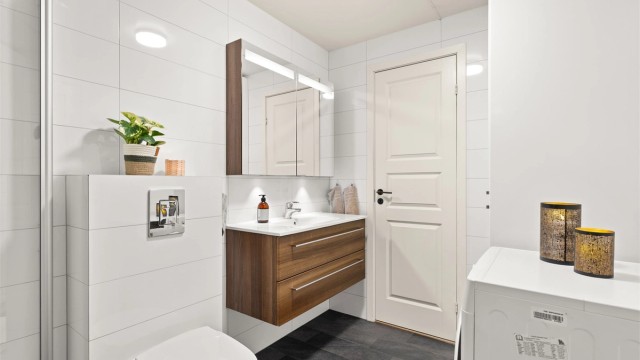 Badet er innredet med vegghengt toalett, servantinnredning med ovenpåliggende servant og armatur, speilskap med overlys og stikkontakt, samt gulvstående høyskap med god oppbevaringsplass. Dusjhjørne med innfellbare dører, samt opplegg til vaskemaskin.