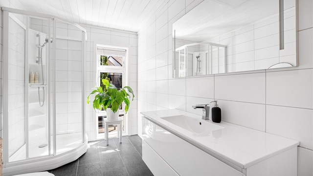 Badet har dusjkabinett, vegghengt toalett samt servant med vask og oppbevaringsplass.
