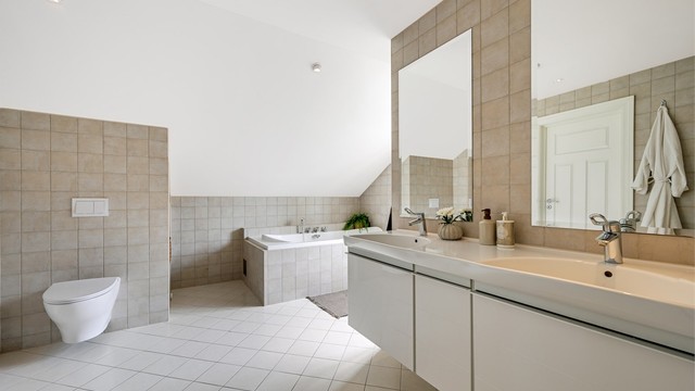 Badet er innredet med dobbel servant, veggmontert toalett, badekar og dusjnisje.