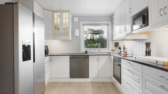 Innredningen har profilerte lyse fronter, laminat benkeplate og vindu over oppvaskkummen.